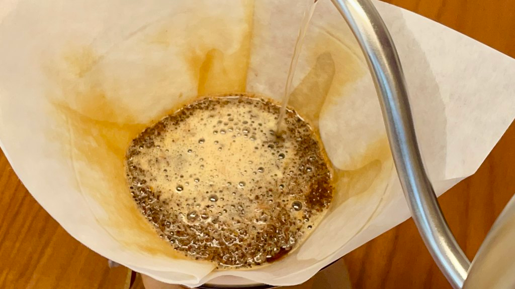 Chemex equipada con un filtro de papel y café recién molido, mientras se le rocía agua caliente desde un hervidor con cuello de cisne.