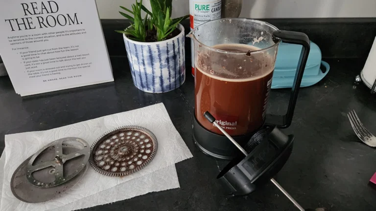 Cafetera prensa francesa con algunas de sus partes desarmadas con café preparado y residuos visibles